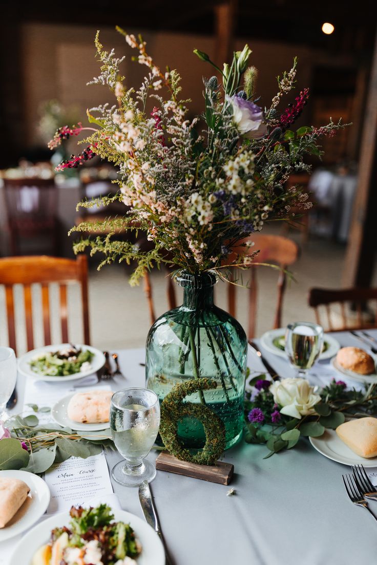 the table is set with plates, silverware and flowers in a green glass vase