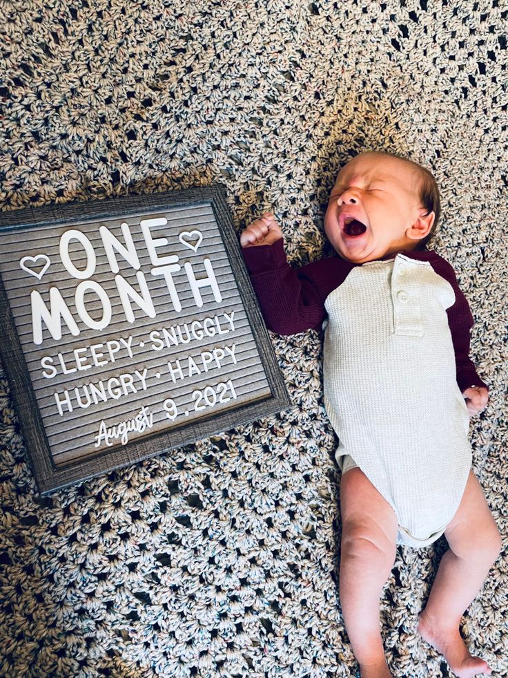 a baby laying next to a sign that says one month sleep, snuggly hungry