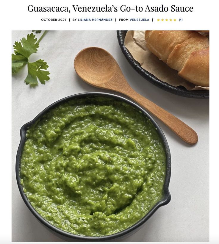 a bowl of guacamole next to a wooden spoon on a white surface