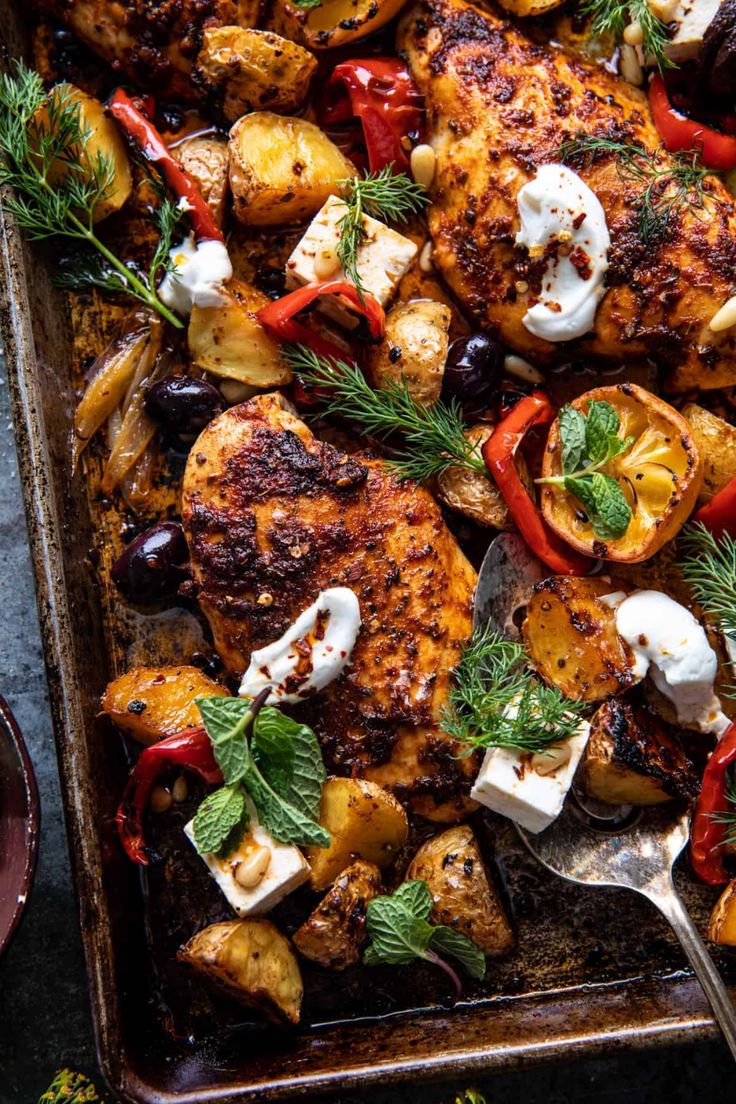 a pan filled with chicken, potatoes and peppers on top of a table next to utensils