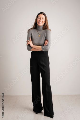 a woman in grey shirt and black pants standing with her arms crossed on the floor