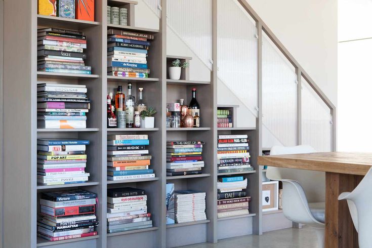 a bookshelf filled with lots of books next to a wooden table and white chairs