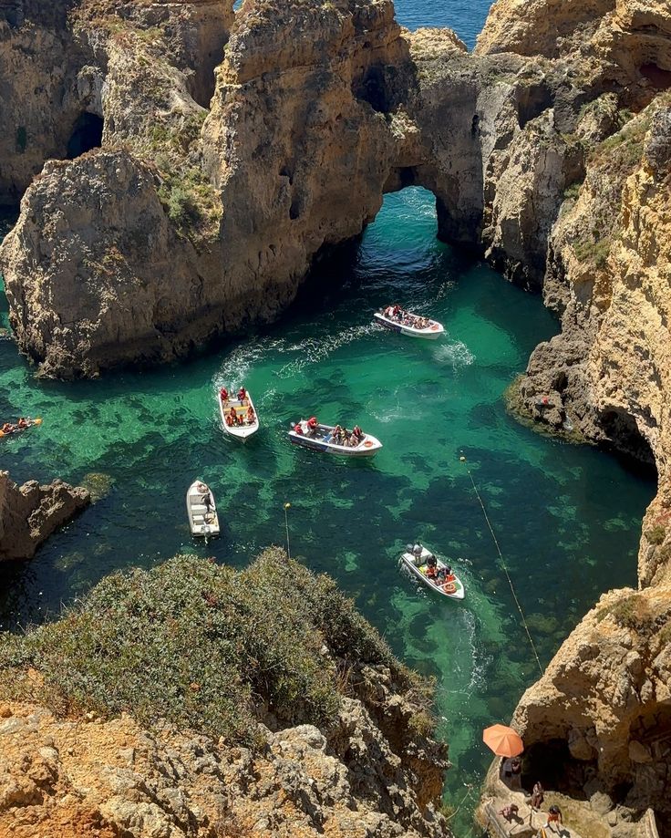 several small boats are in the clear blue water near some rocky cliffs and an arch