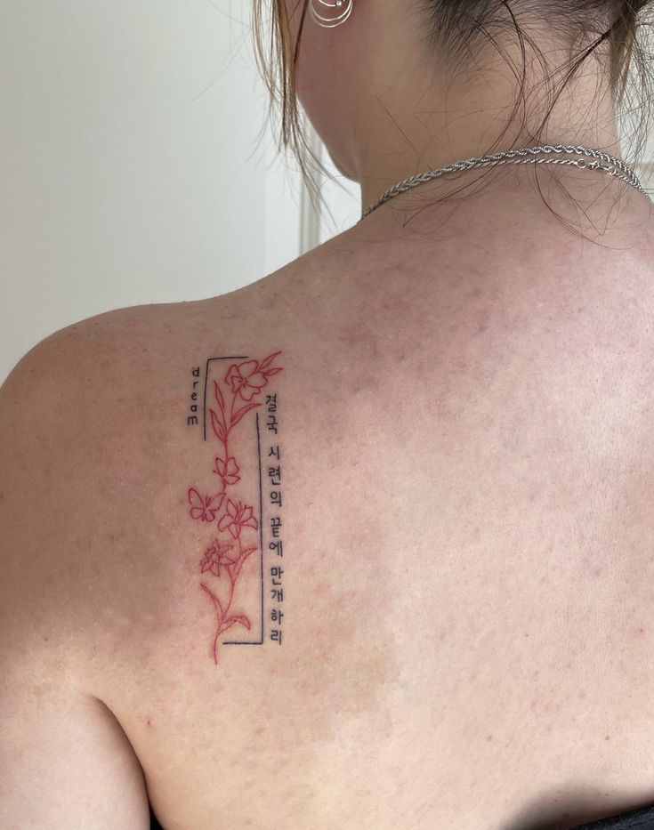 the back of a woman's shoulder with chinese writing and flowers tattooed on it