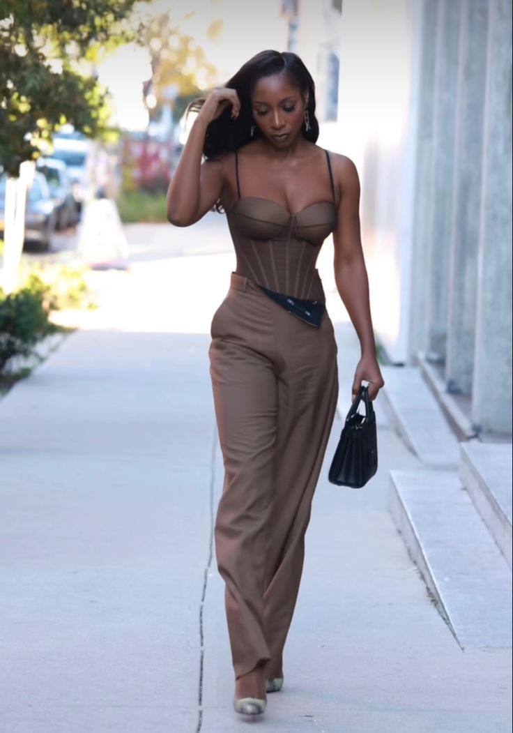 Woman walking in New York wearing a brown corset jumpsuit and a black hand bag Corset Top Jumpsuit, Brown Semi Formal Outfits For Women, Black And Brown Dress, Brown And Gold Outfits For Black Women, Neutral Party Outfit, Nude Corset Outfit, Corset Jumpsuit Outfit, Brown Corset Top Outfit, Nude Outfits For Black Women