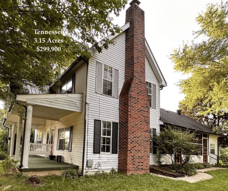 a white house with black shutters and a red brick chimney in the front yard