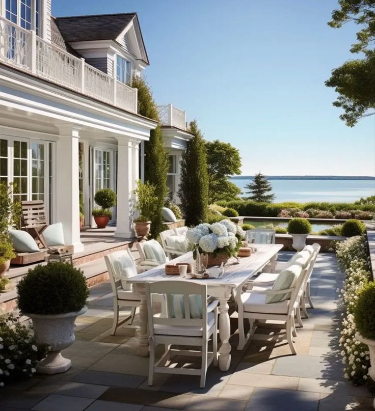 an outdoor dining table and chairs on a patio next to the ocean in front of a house