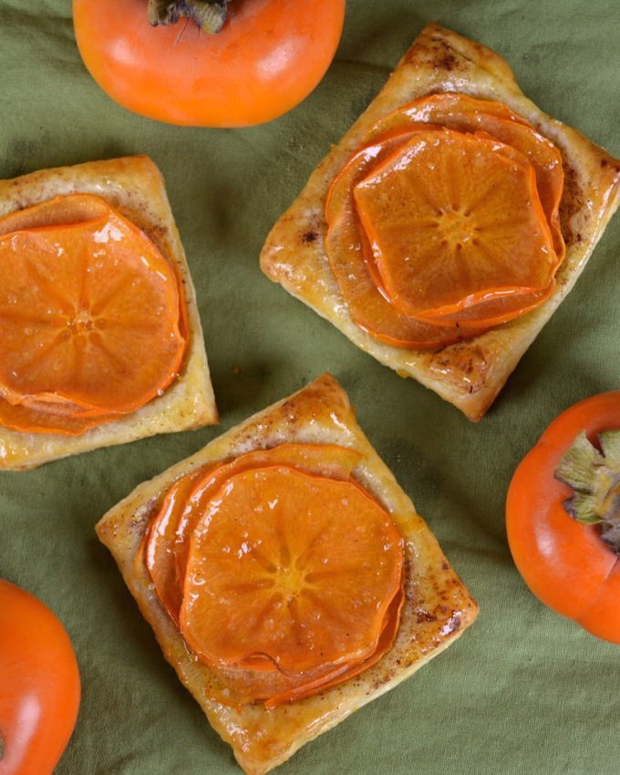 four pieces of bread with orange slices on them and some tomatoes in the background next to each other