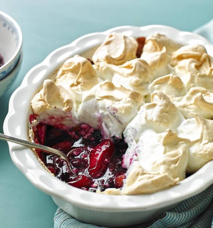 a pie with whipped cream and cherries in a white dish on a blue table