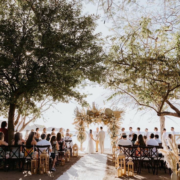 an outdoor wedding ceremony with people sitting at the end of the aisle and trees in the background