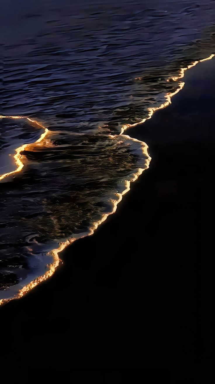 the ocean waves are coming in to shore at night with light reflecting off the water