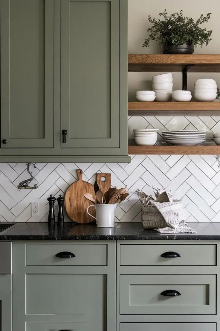 a kitchen with green cabinets and white tile backsplash, black countertops and wooden shelves