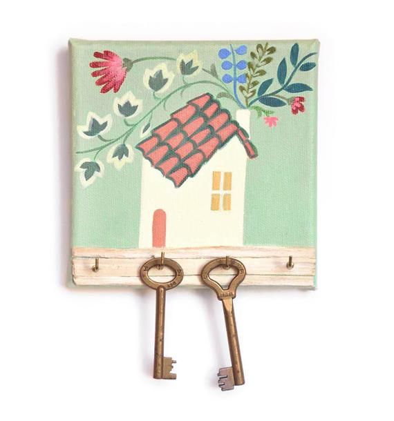 two keys hang from a key holder with a house painted on the wall behind it