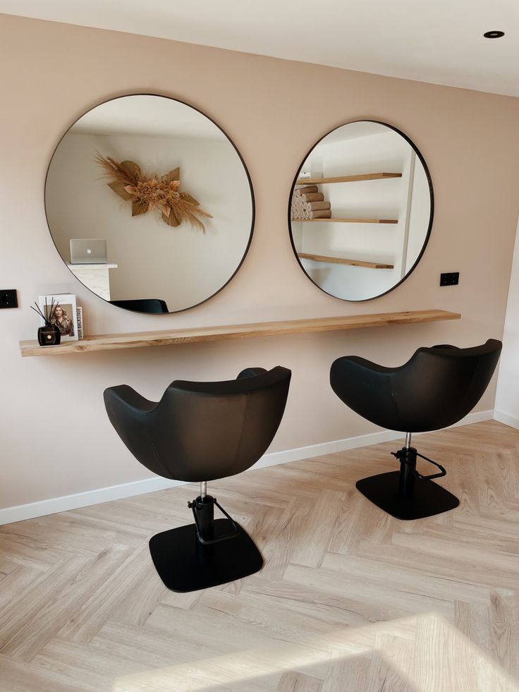 two mirrors on the wall above black chairs