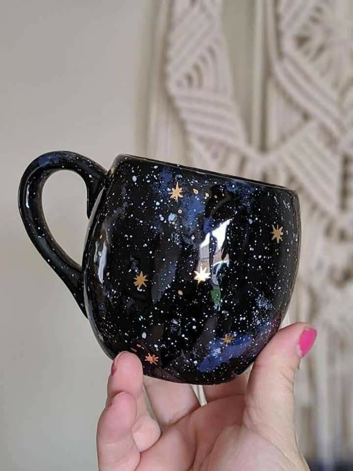 a hand holding a black coffee cup with stars on the bottom and a unicorn painted on it