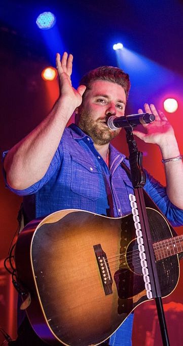 a man singing into a microphone while holding a guitar in front of him on stage