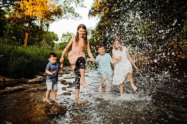 three children are playing in the water with their mom and dad while another child is running behind them