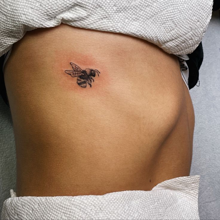 a woman's stomach with a small bee tattoo on the side of her belly