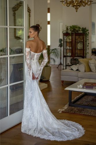 a woman in a white wedding dress standing by a glass door with her back to the camera