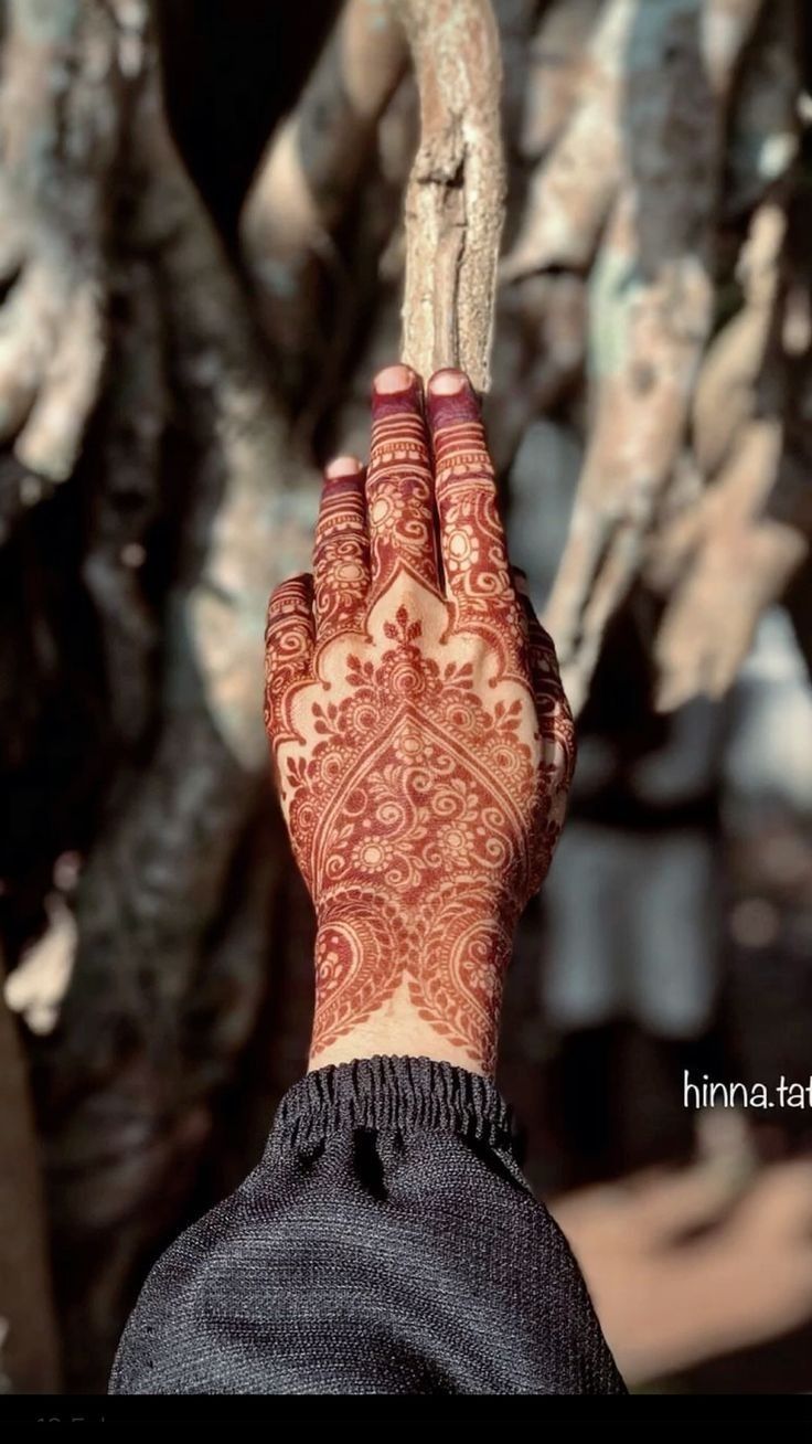 a woman's hand with henna tattoos on it holding a stick in front of a tree