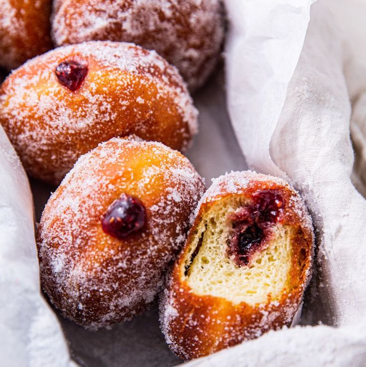 powdered sugar covered donuts with cranberries in a white basket on a table