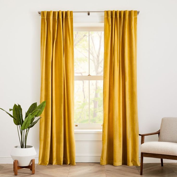 a living room with a chair and window covered in yellow drapes next to a potted plant