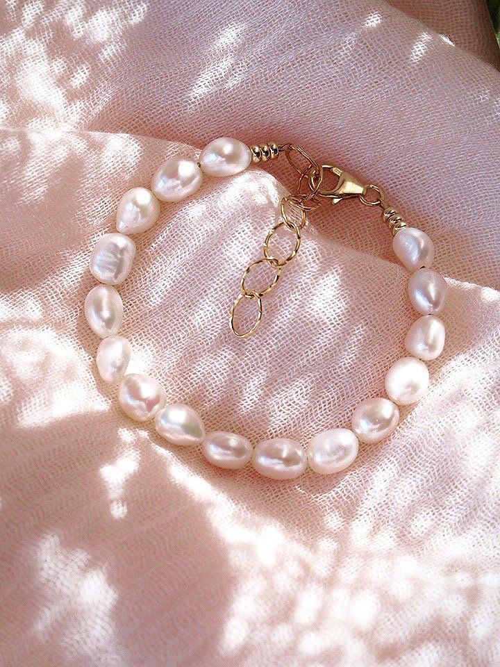 This shimmering porcelain white freshwater pearl bracelet is a must have staple. Wear this gold pearl bracelet to remind yourself of the soothing sands of Hawaii.✦ DETAILS ✦✧ Name: Ala (AH lah) - fragrant; esteemed.✧ Adjustable Length from 6.5"-8".✧ White 6-7mm Freshwater Pearls.✧ 18kt Gold Filled with lobster clasp.✧ All Ke Aloha Jewelry pieces come packaged thoughtfully, beautifully, and ready for gift giving. Luxury Minimalist Chain Bracelet With Oyster Design, Luxury Dainty White Pearl Bracelet, White Charm Bracelet For Beach, Feminine Pearl Drop Bracelets, Everyday Pearl Bracelets With Pearl Drop, Timeless White Bracelet With Pearl Charm, Elegant Everyday Cream Jewelry, Timeless Pearl Bracelet With Pearl Drop As Gift, Everyday Pearl Bracelet With Pearl Drop