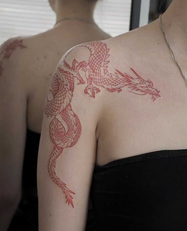 a woman with a dragon tattoo on her arm and shoulder is looking at herself in the mirror