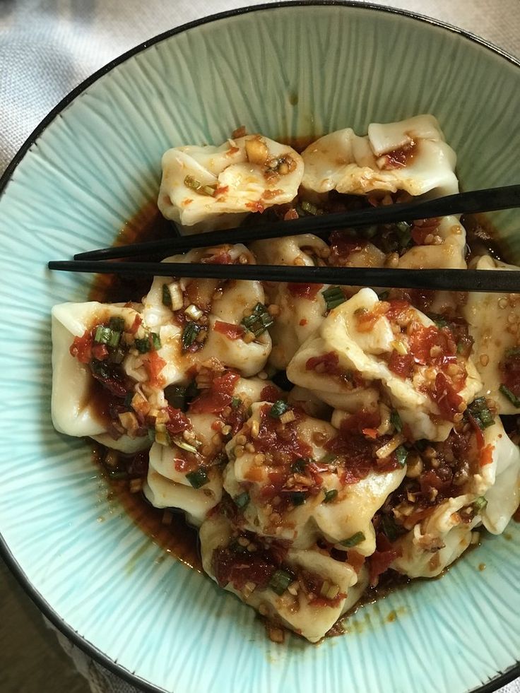 a blue bowl filled with dumplings and chopsticks