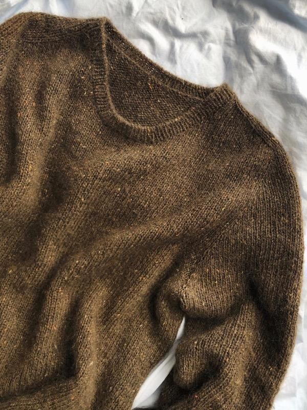 a brown sweater laying on top of a white sheet