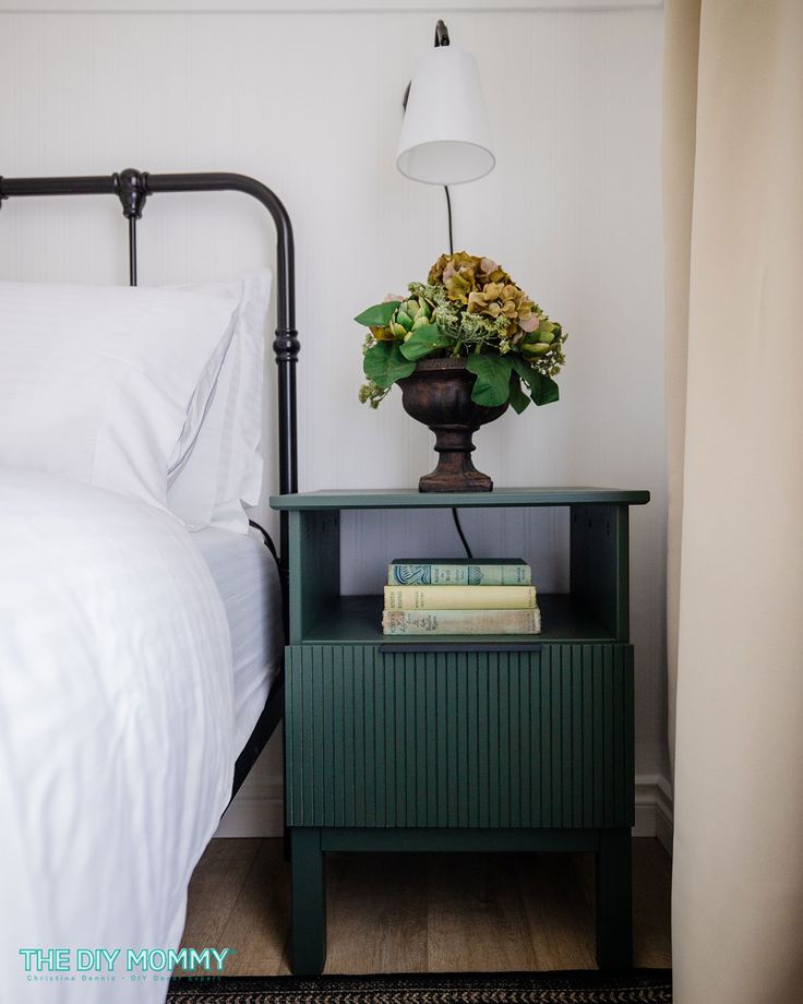 a nightstand with flowers on it next to a bed