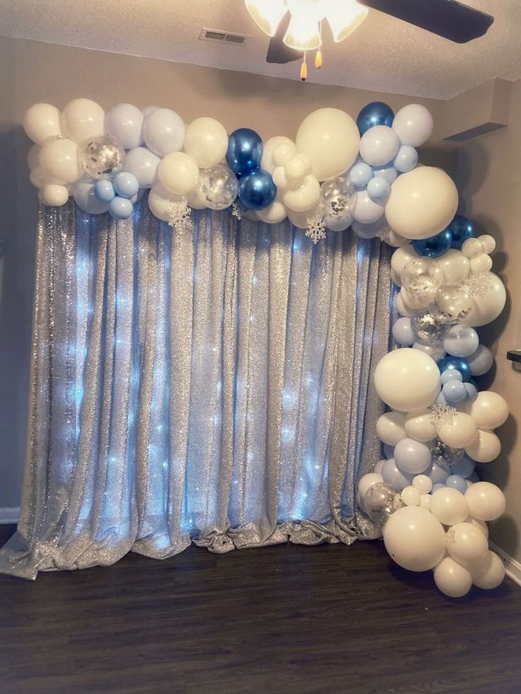 an arch made out of balloons and streamers in front of a window with curtains