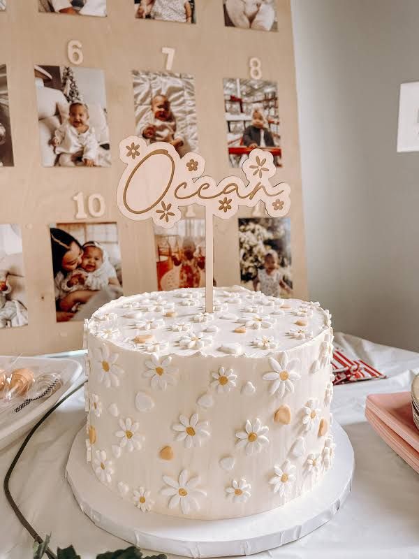 a white cake sitting on top of a table covered in photos and flowers next to a wooden sign