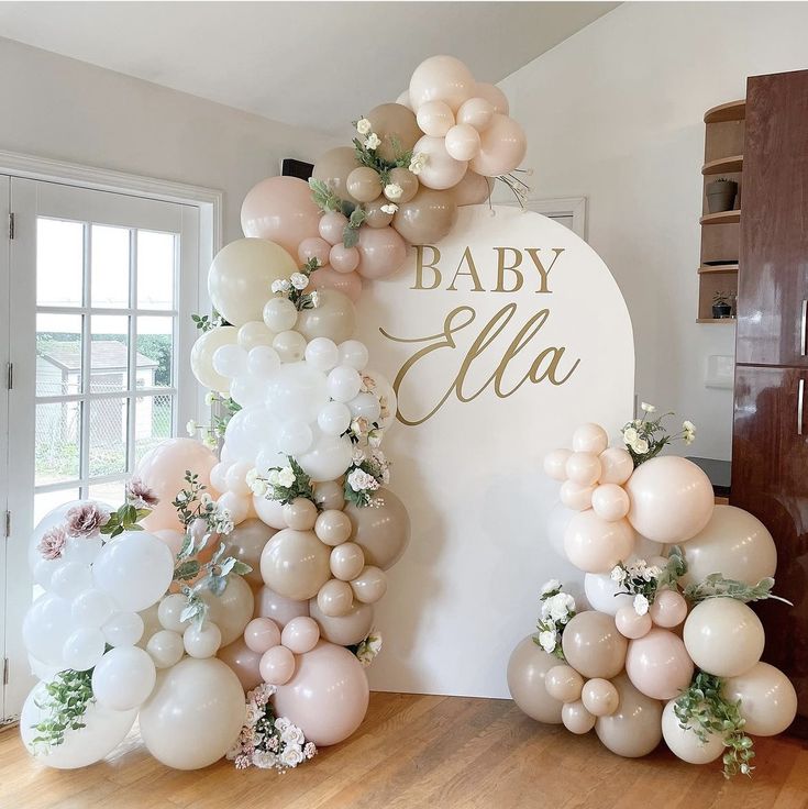 a baby shower sign with balloons and greenery on it in front of a wooden floor