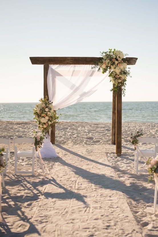 an outdoor ceremony setup on the beach with white flowers and greenery draped over it