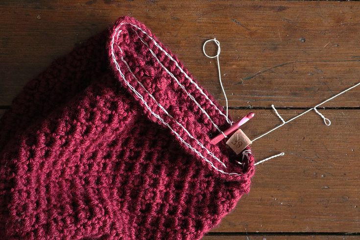 a close up of a knitted object on a wooden table with pins and needles