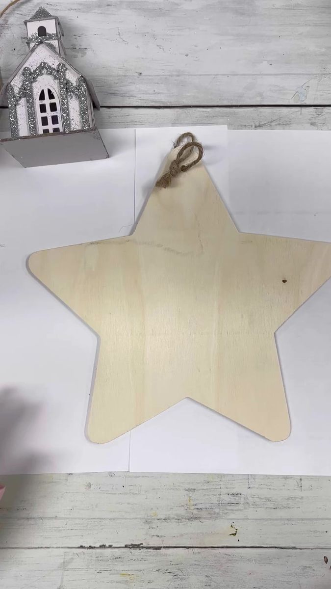 a wooden star ornament hanging on a white wall next to a small house