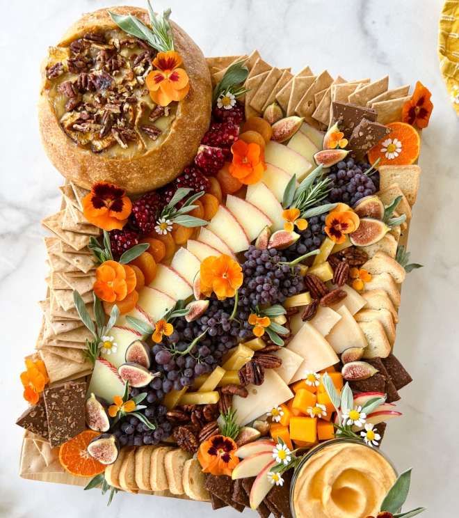 an assortment of fruits and cheeses arranged on a platter with crackers, nuts, dried flowers