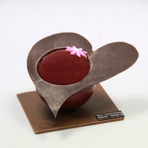 a heart shaped bowl with a pink flower in it sitting on top of a plaque