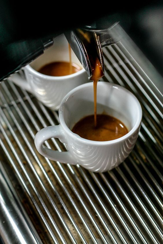 espresso being poured into two white mugs on a coffee machine with stainless steel grates