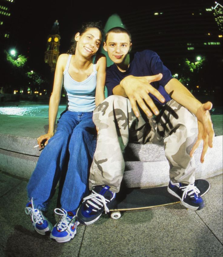 a man and woman are sitting on a skateboard in front of a fountain at night