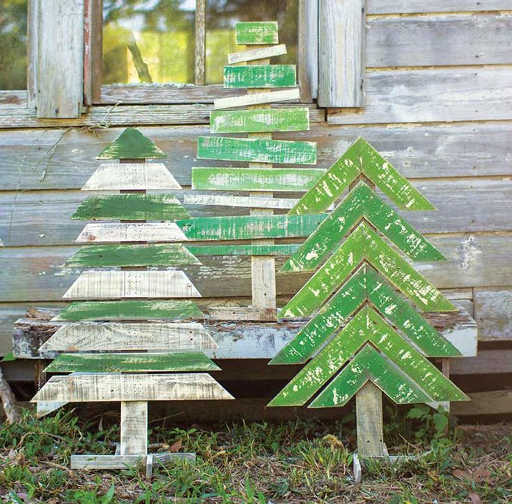 a wooden christmas tree sitting in front of a window on top of a grass covered field