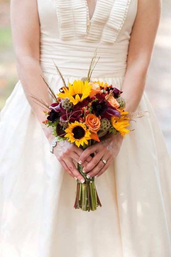 a bride holding a bouquet of sunflowers and other flowers on her wedding day