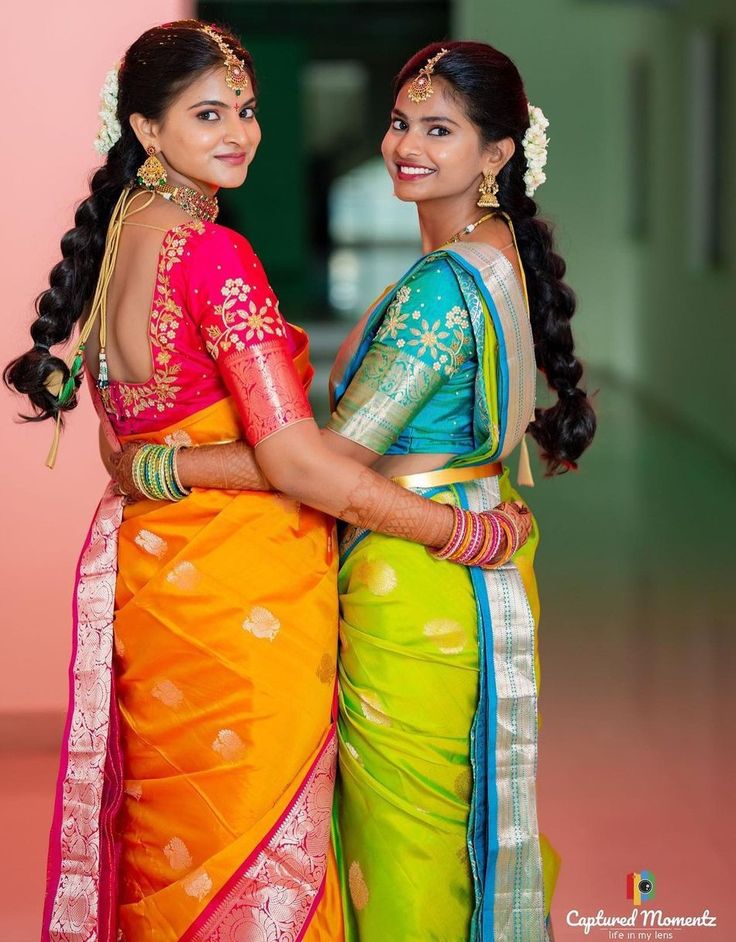 two women dressed in colorful sari standing next to each other with their arms around each other