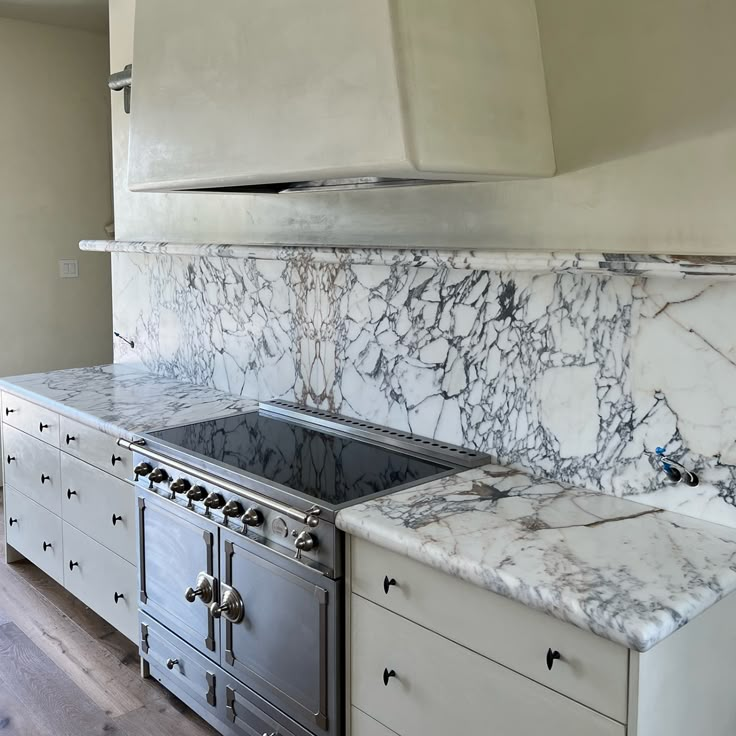 a kitchen with marble counter tops and stainless steel oven hood over the stove, along with white cabinets