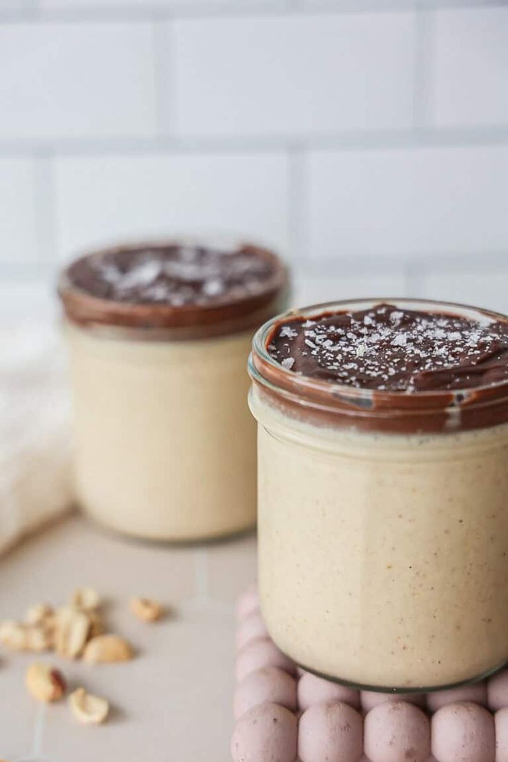 two jars filled with desserts sitting on top of a white counter next to nuts