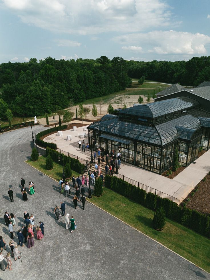 a group of people standing in front of a glass building on top of a lush green field