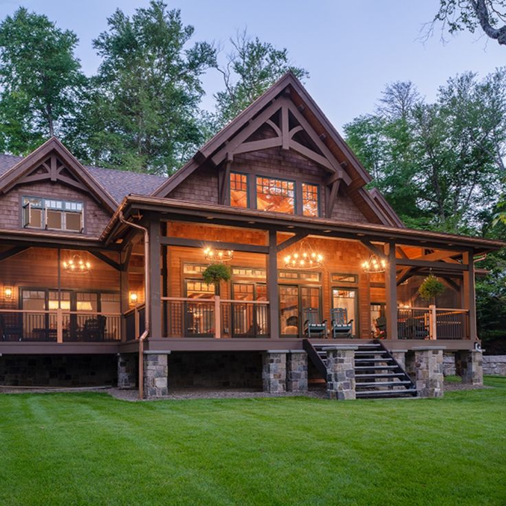 a large house with lots of windows and lights on the front porch, surrounded by lush green grass