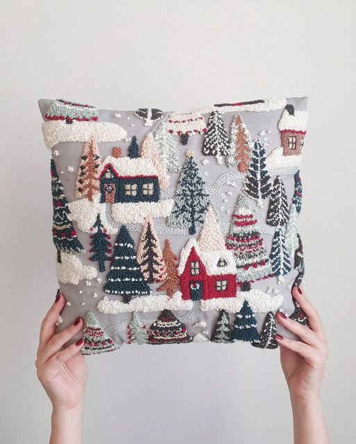 someone is holding up a pillow with christmas trees and houses on it in front of a white wall