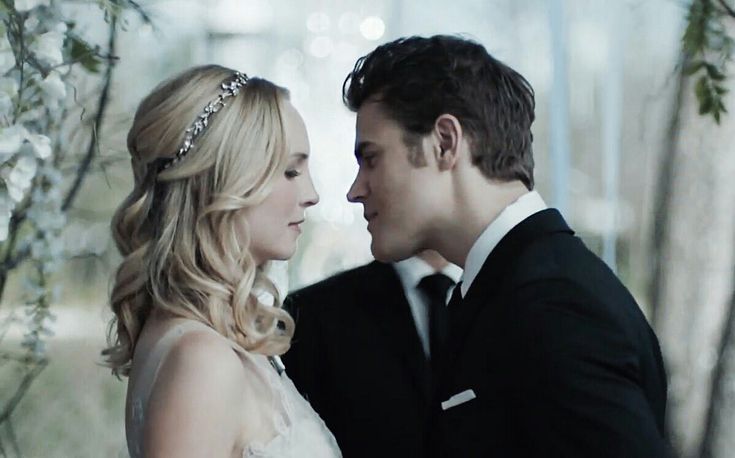 a bride and groom kissing in front of an arch with flowers on the wall behind them